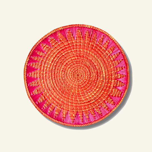 Orange and pink Sikki grass handwoven round mat on a Dhoop Cream background